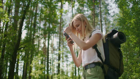 A-traveler-in-the-forest-with-a-backpack-walks-along-the-path-and-looks-at-the-mobile-phone-screen